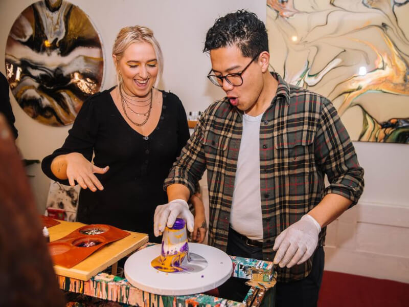 A woman teaching a man how to create fluid art